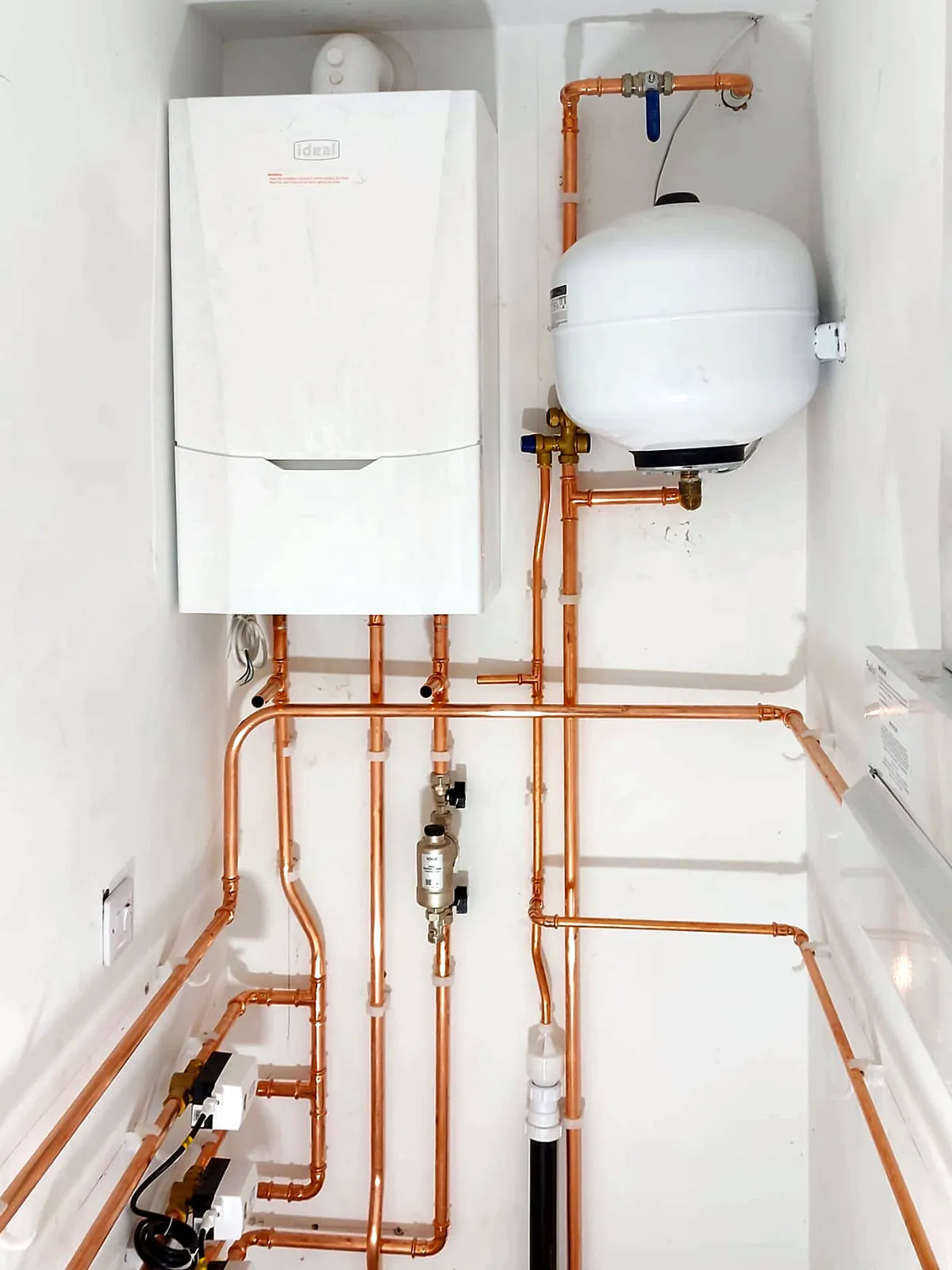 The finished plant cupboard: an Ideal boiler, an expansion vessel and copper pipework run in clipped, square lines across the walls.